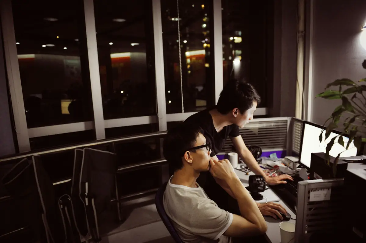 Two people at a desk late at night, city lights outside